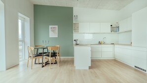 Une cuisine moderne avec des meubles blancs, un coin repas comprenant une table et des chaises, et un mur d’accent vert.
