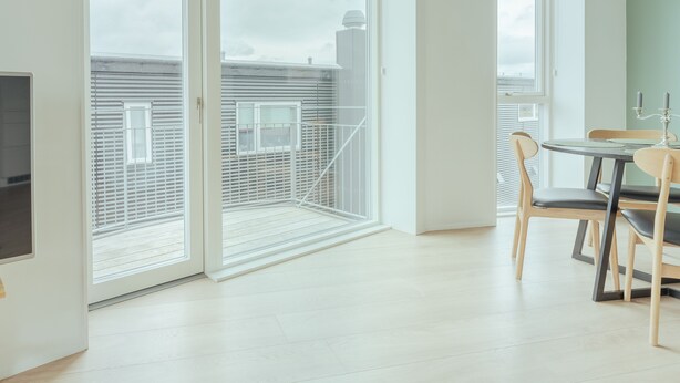 Un appartement moderne doté d’une porte-fenêtre coulissante donnant sur un balcon, d’un coin repas avec une table et des chaises, et offrant une vue sur le paysage urbain.