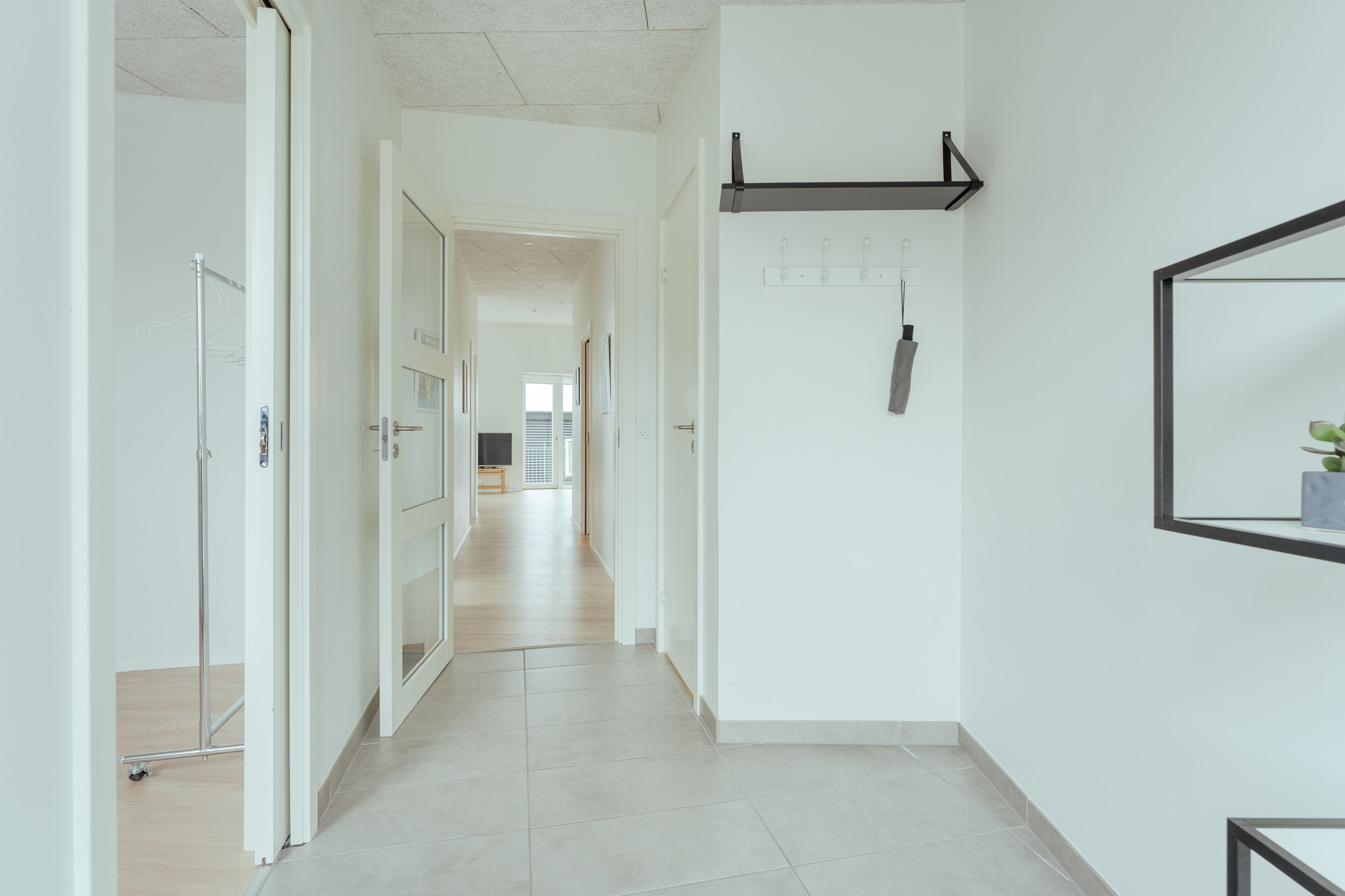 A hallway with a tiled floor, a coat rack, and a door leading to another room.