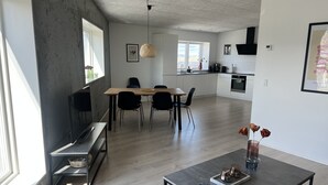 Een moderne woonkamer met een eetgedeelte, keuken en grote ramen.
