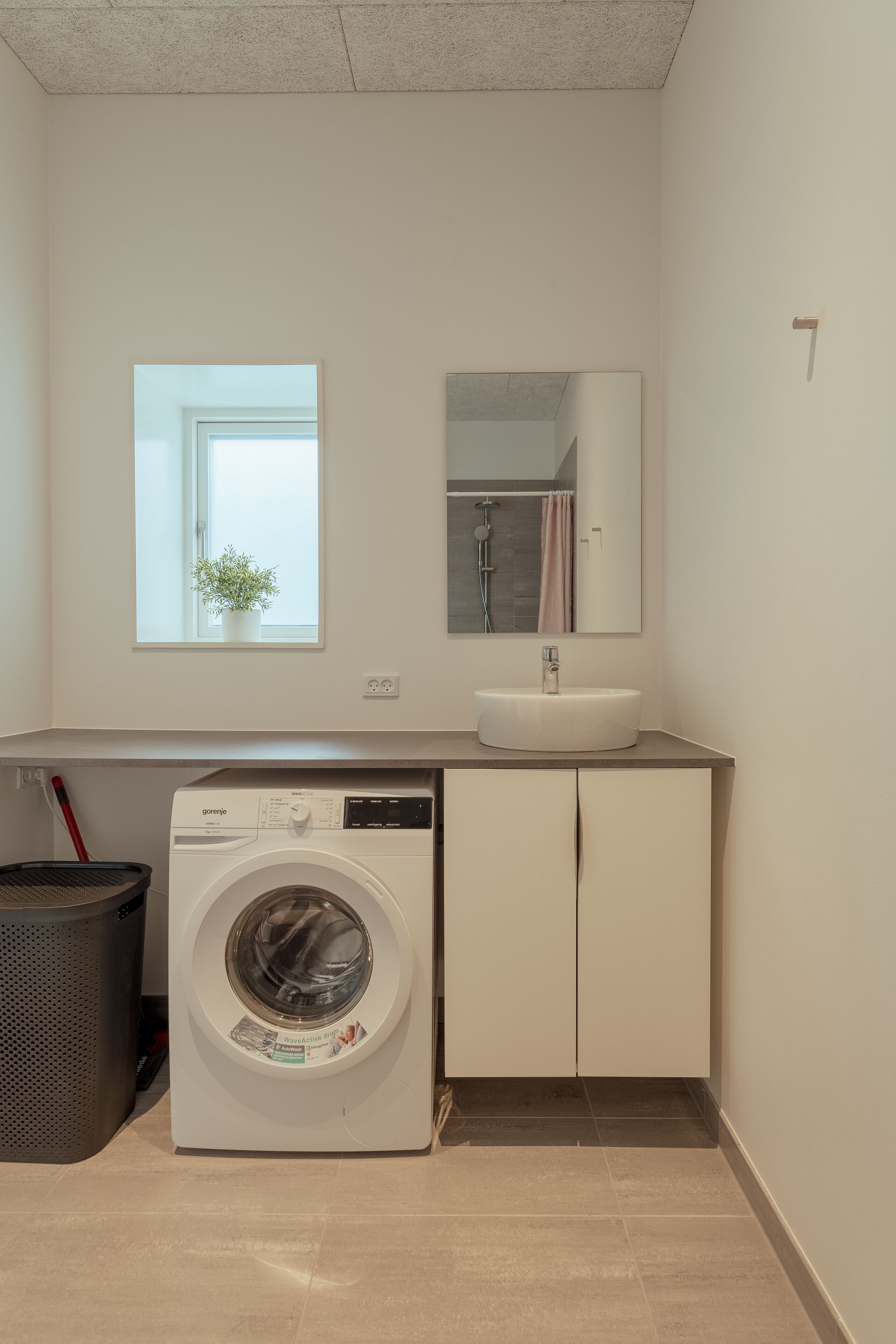 A compact laundry room with a front-loading washing machine, a sink, and a mirror above it.