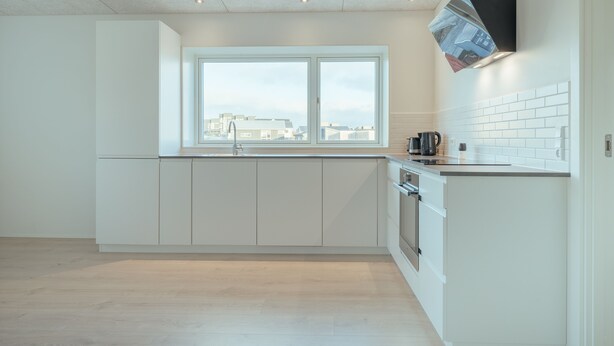 Een moderne keuken met witte kasten, een raam met stadszicht en een zwarte afzuigkap.