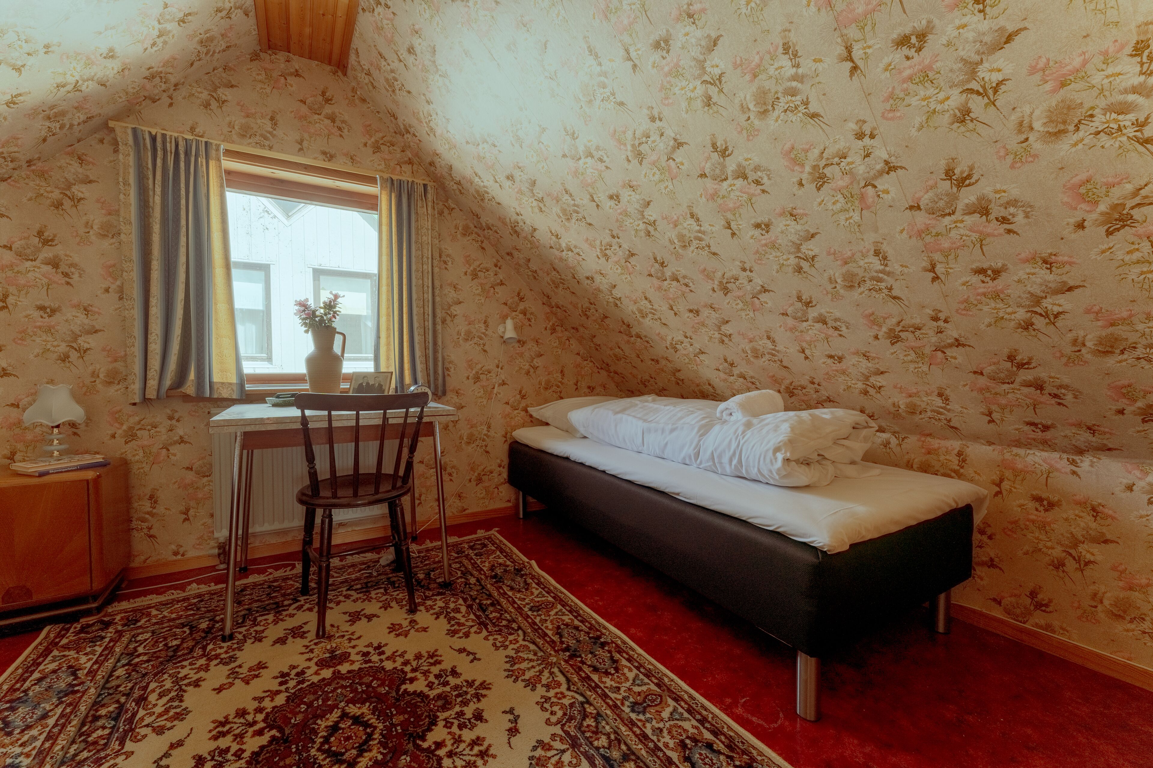 Un dormitorio con cama, escritorio, silla y ventana con cortinas.