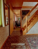 Eine Holztreppe führt zu einem Essbereich mit einem gemusterten Teppich und einem gerahmten Schild an der Wand.