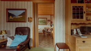 A cozy room with a leather armchair, a wooden desk, and a bookshelf filled with books and decorative items. - Charming 3 Br Home | Scenic Village | Nature (Eiði)