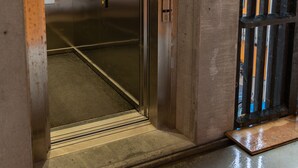 An elevator with a metallic interior and a glass door, leading to a corridor with a concrete floor. - New 2Br Apartment | Sea View (Tórshavn)