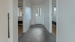 A hallway with a tiled floor, a door at the end, and a bed visible in the background. - New 2Br Apartment | Sea View (Tórshavn)
