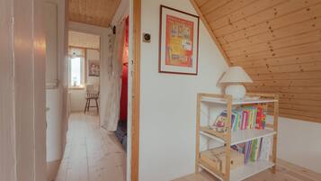 A room with a sloped ceiling, a wooden bookshelf with books, a framed poster on the wall, and a door leading to another room.