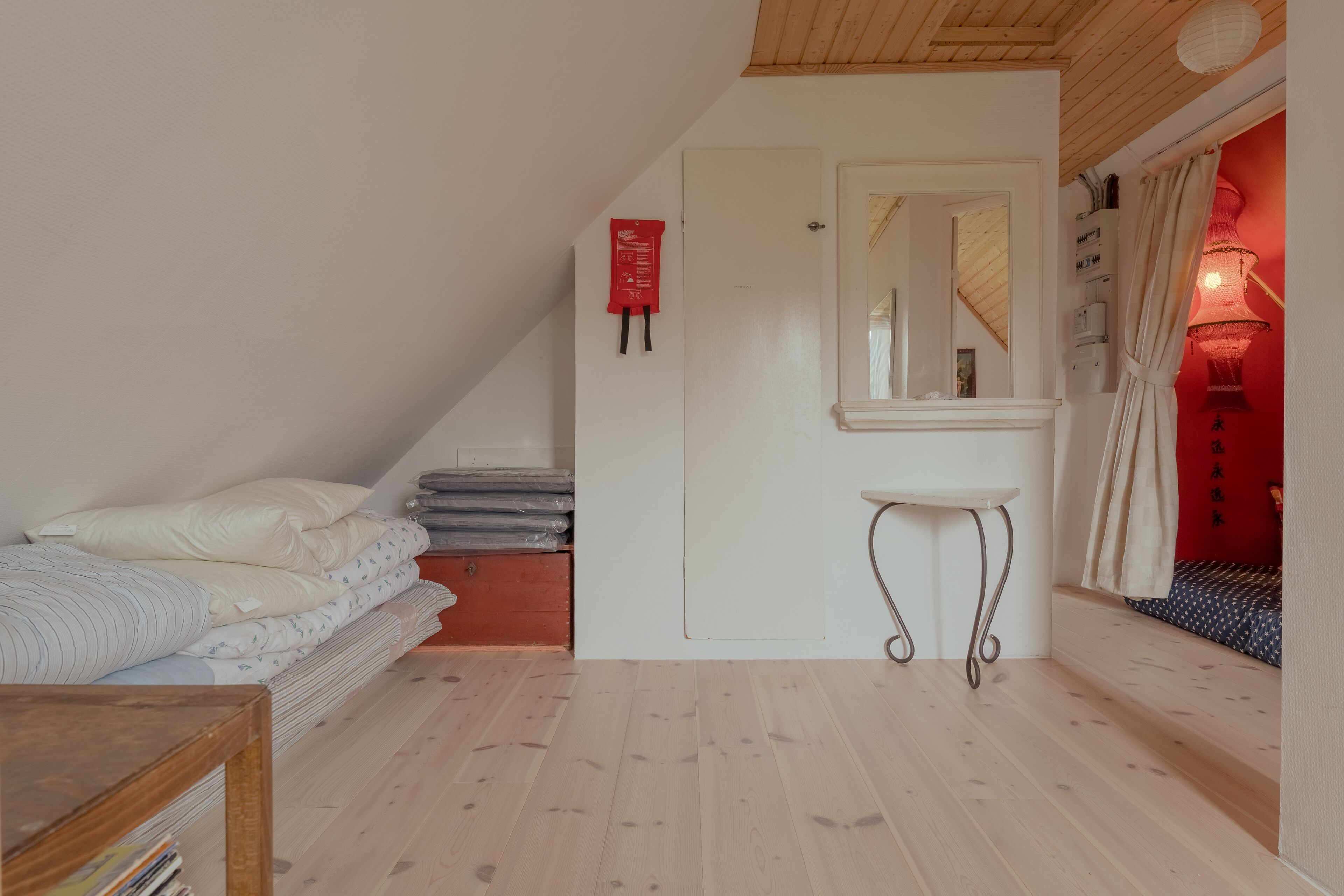 Un dormitorio con una cama, una mesita de noche pequeña, una puerta blanca y un espejo.