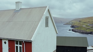 Una casa costera con puerta roja y paredes blancas, con vistas a un litoral rocoso y al mar.