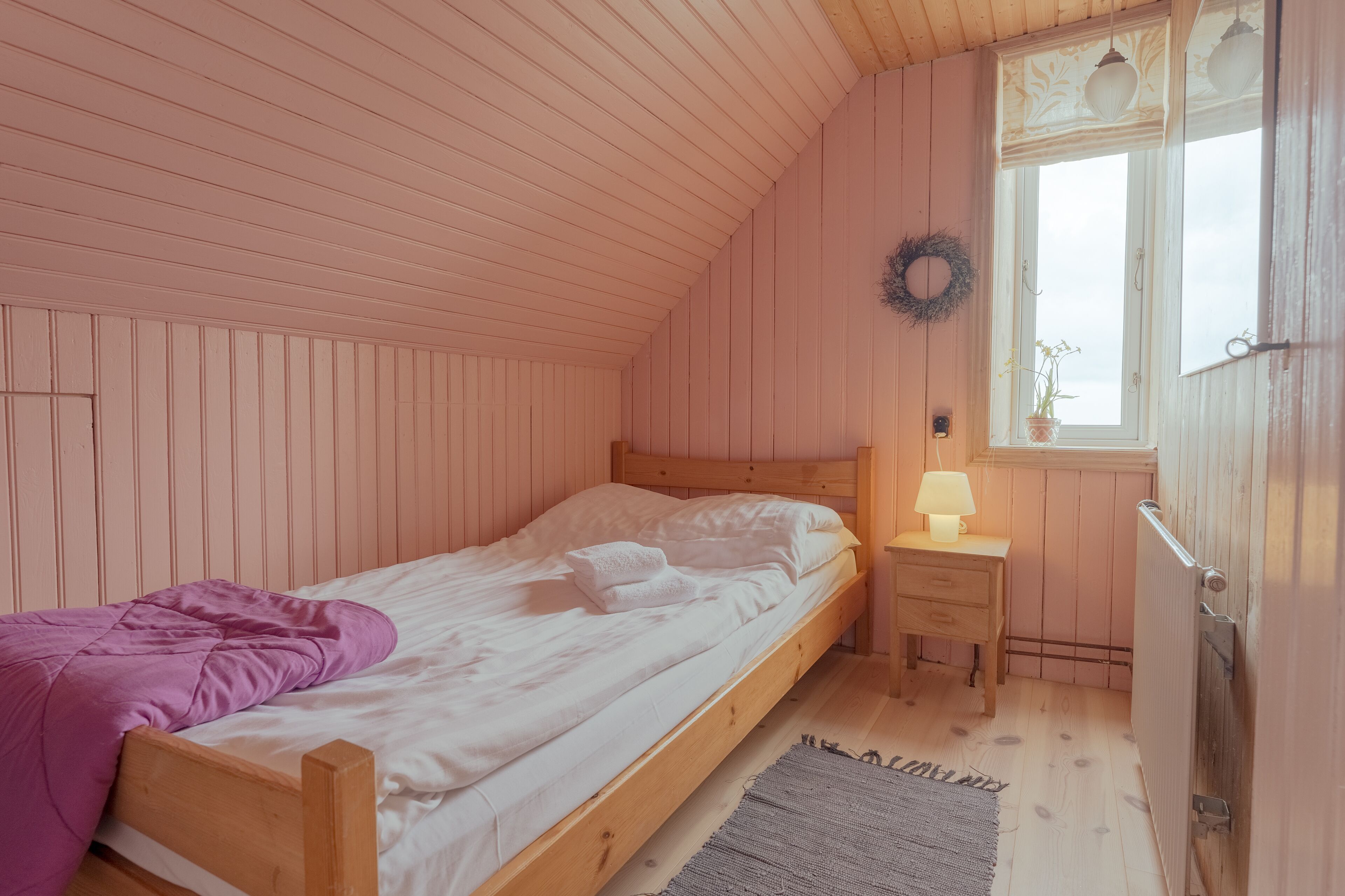 Un dormitorio acogedor con una cama de madera, una mesita de noche con una lámpara, una ventana adornada con un adorno y un suelo de madera.