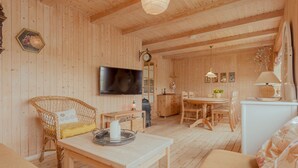 Un interior de madera acogedor con comedor, televisor y sillón de mimbre.