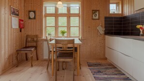 Un interior de madera con una mesa y sillas de comedor, una ventana con vistas, y una zona de cocina con salpicadero de baldosas negras.