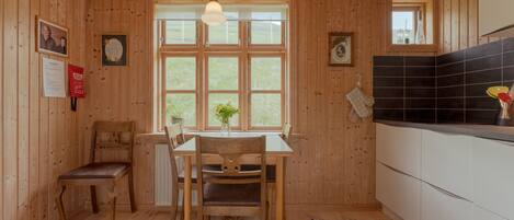 Un intérieur en bois comprenant une table et des chaises, une fenêtre offrant une vue agréable et un coin cuisine avec un dosseret de carrelage noir.