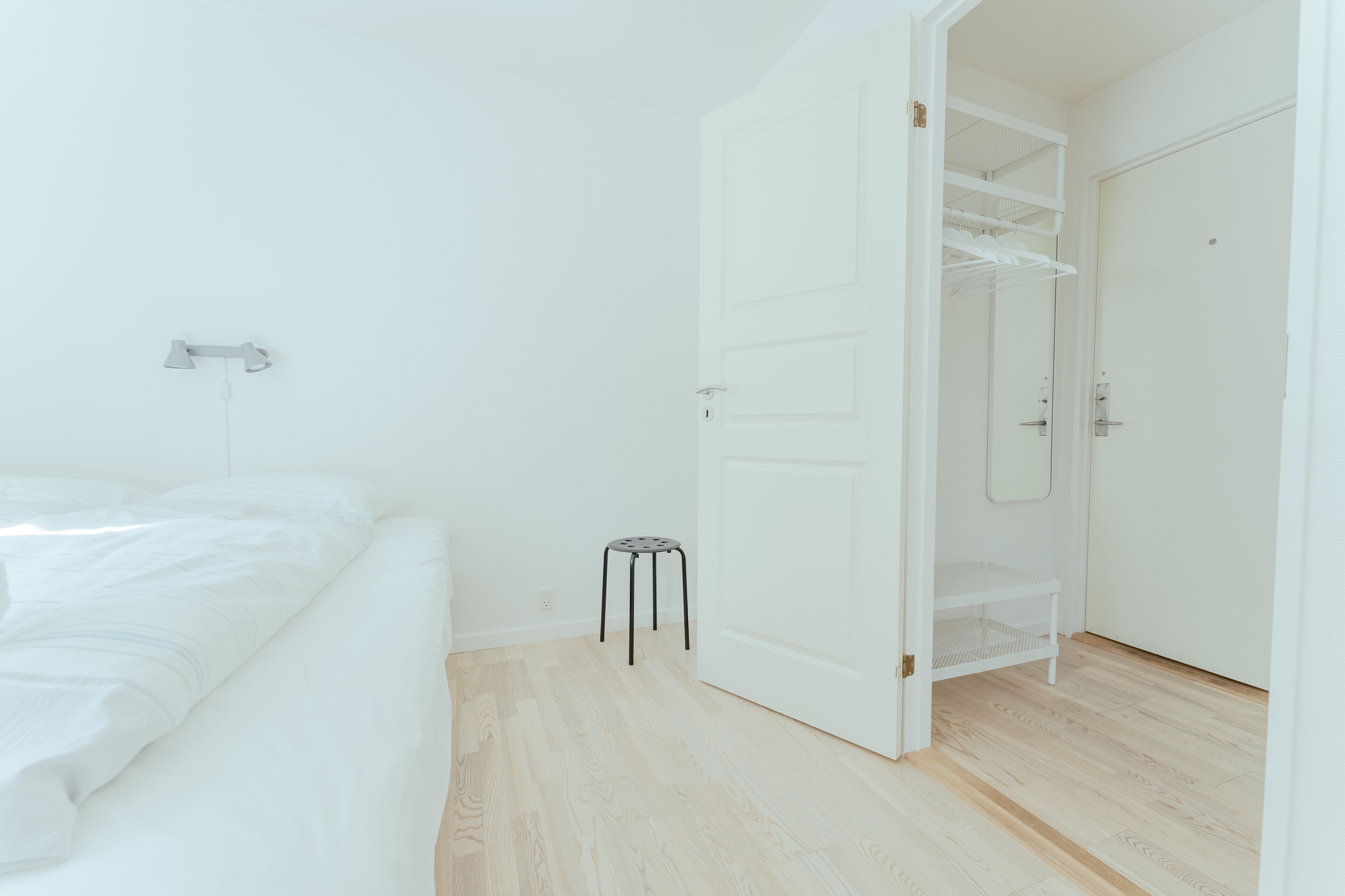 A bedroom with a bed, a small stool, and a closet with a mirror.