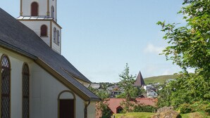 A church with a clock tower, a clear sky, and a grassy area with a stone monument. - 1 Bedroom Apartment | Central | Tórshavn (Tórshavn)