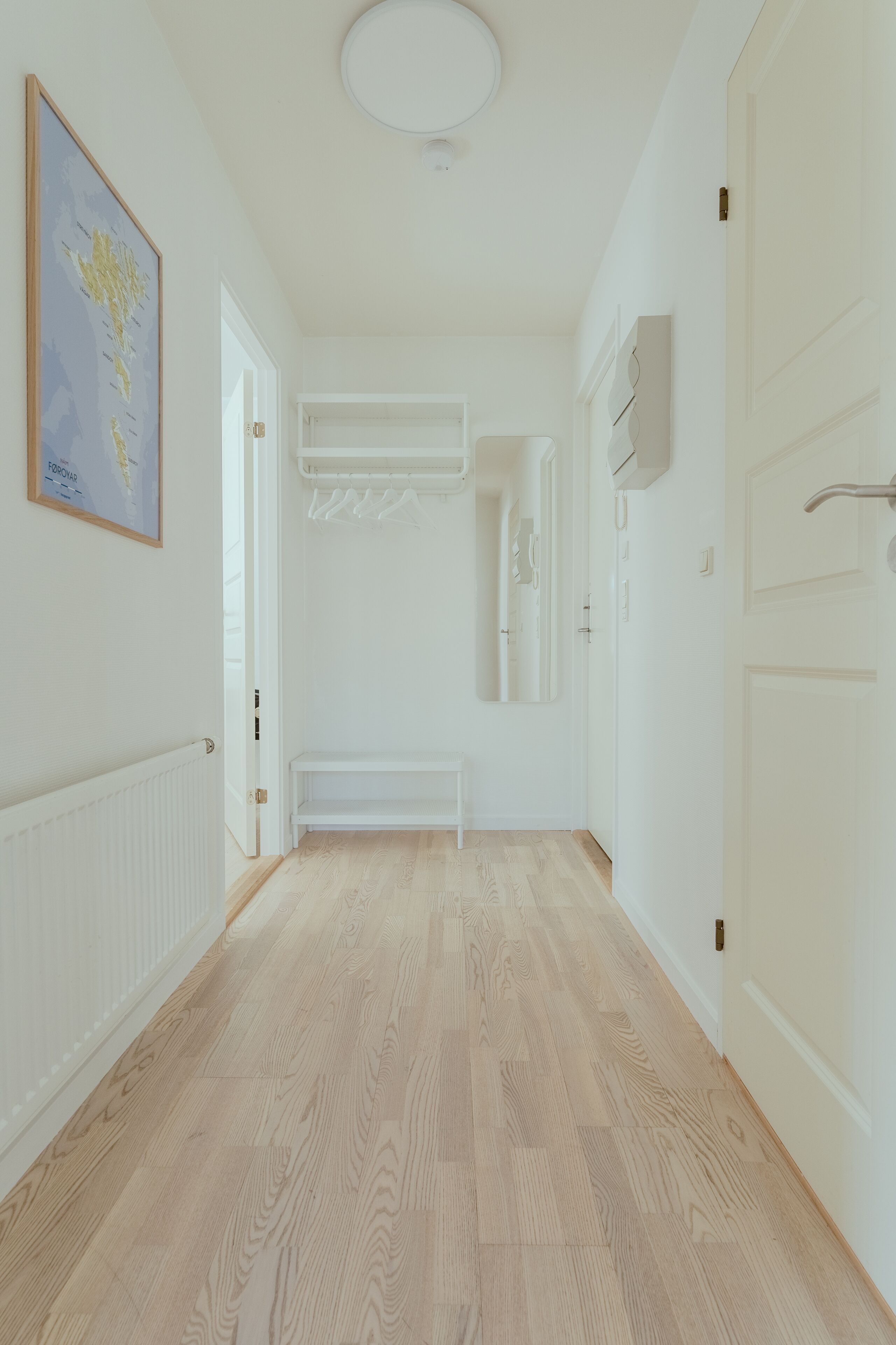 A hallway with a wooden floor, white walls, a framed map, and a white bench.