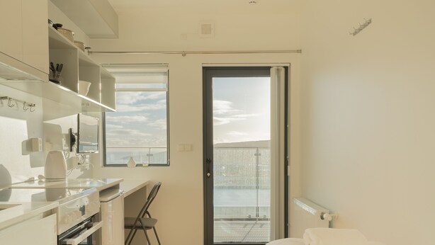 A modern hotel room with a kitchenette, a bed, a desk, and a balcony with a view. - Stylish Studio Apartments (Tórshavn)