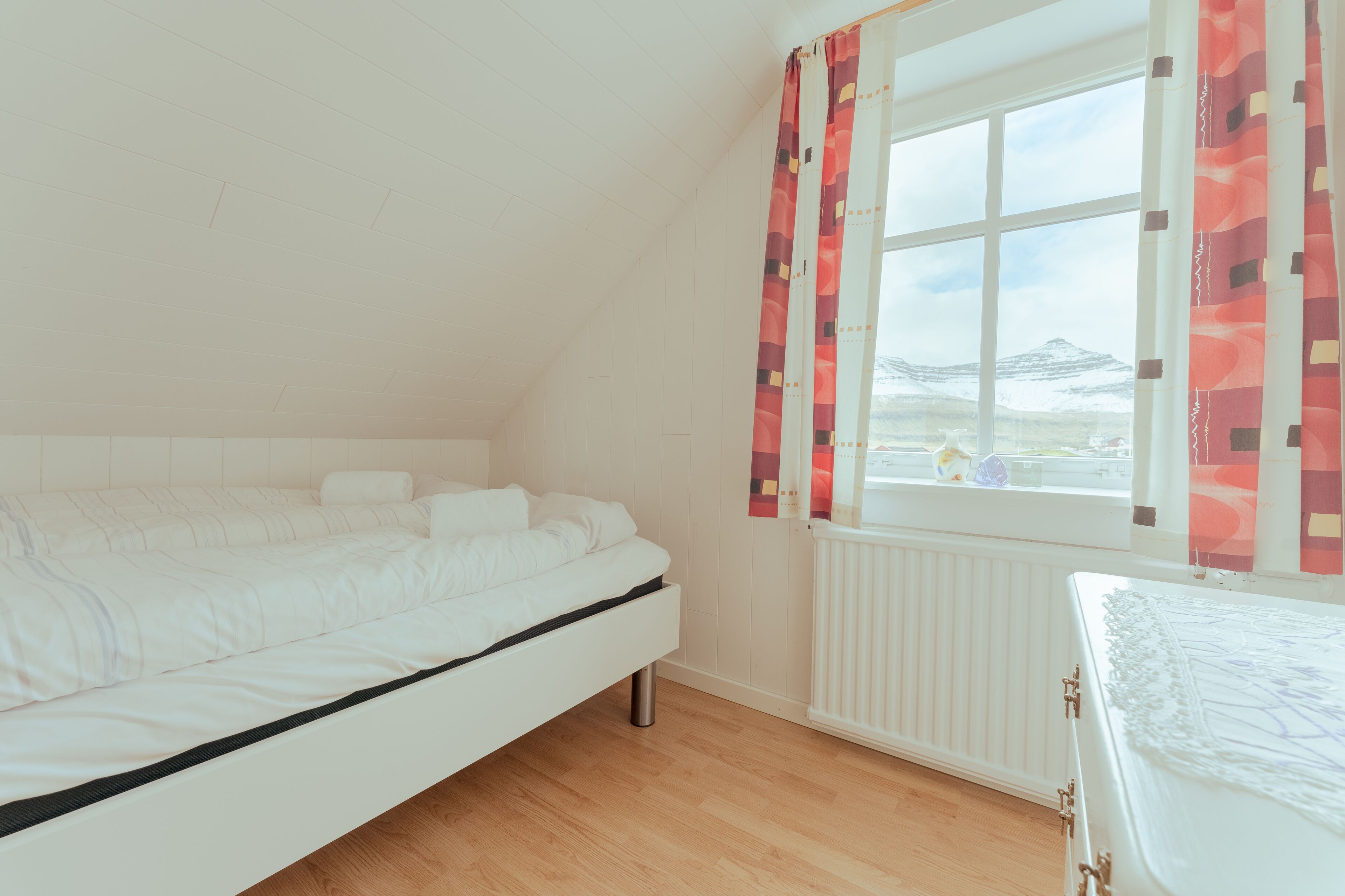 A bedroom with a bed, a window with curtains, and a view of mountains.