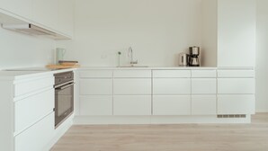 A modern kitchen with white cabinetry, a built-in oven, a coffee maker, and a kettle on the counter. - Nordic Swan Aparthotel | Seaview| Stunning 2Br Apt (Tórshavn)