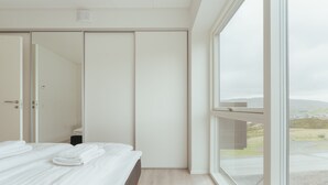 A modern bedroom with a large bed, a wardrobe, and a window offering a view of the outdoors. - Nordic Swan Aparthotel | Seaview| Stunning 2Br Apt (Tórshavn)