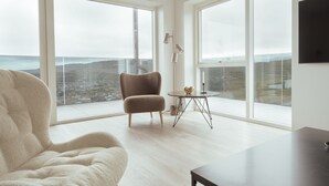 A spacious room with large windows, a comfortable armchair, a small round table, and a minimalist decor. - Nordic Swan Aparthotel | Seaview| Stunning 2Br Apt (Tórshavn)