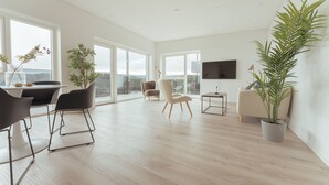A spacious living room with a dining area, large windows, and a flat-screen TV. - Nordic Swan Aparthotel | Seaview| Stunning 2Br Apt (Tórshavn)
