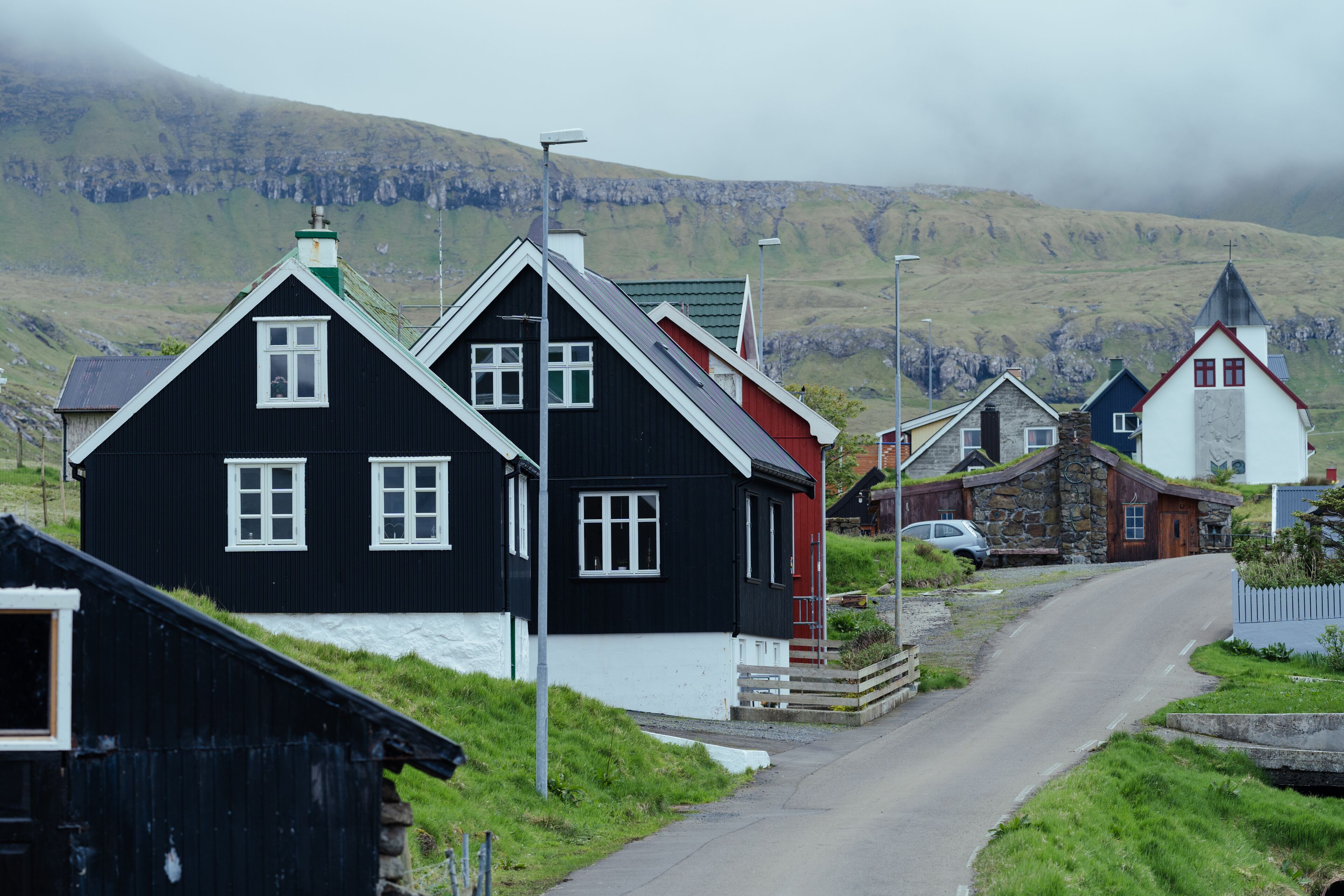 A narrow road in a rural area with traditional black and white houses, a stone building, and a church with a red roof.