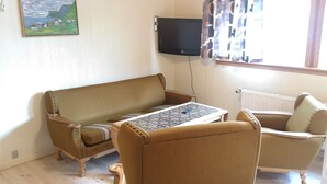 A living room with a sofa, armchair, and a table with a patterned tablecloth. - 1 Br Apt | Selatrað | Free Parking (Selatrað)
