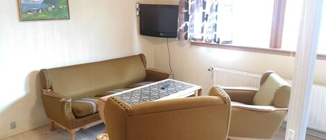 Een woonkamer met een bank, fauteuil en een tafel met een tafelkleed met patroon.