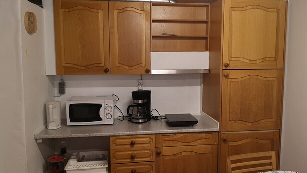 A compact kitchen with wooden cabinets, a microwave, a coffee maker, and a small countertop. - 1 Br Apt | Selatrað | Free Parking (Selatrað)