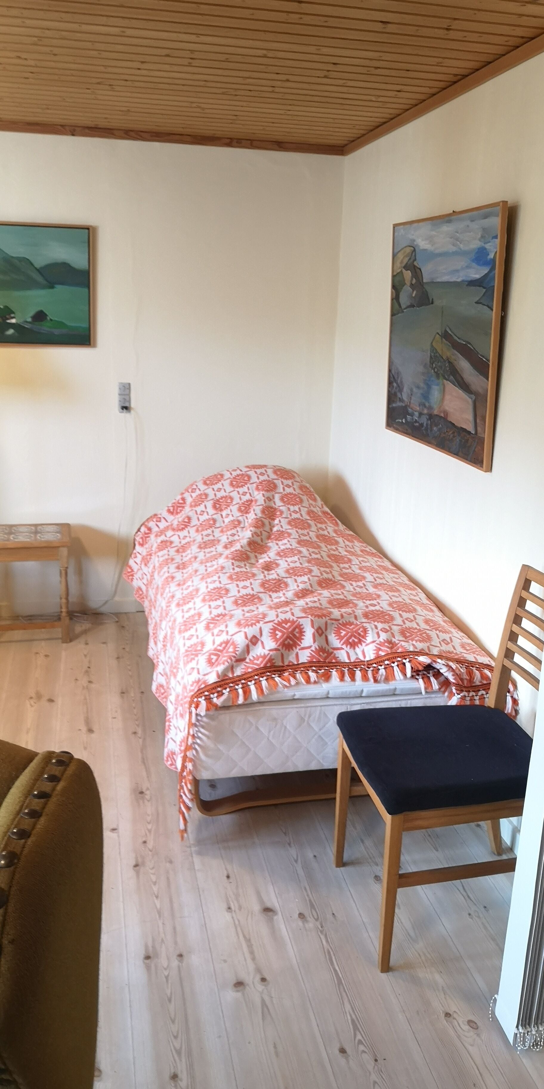 A small, cozy room with a single bed, a wooden chair, and a desk.