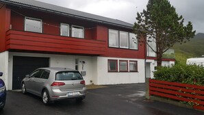 A red and white building with a garage, two parked cars, and a tree in front. - 1 Br Apt | Selatrað | Free Parking (Selatrað)