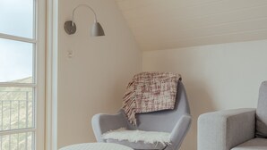 Una habitación con un sillón gris, un reposapiés blanco, un felpudo blanco y un sofá gris.