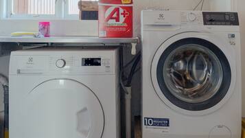 A laundry area with two washing machines, a window, and a shelf with cleaning supplies.