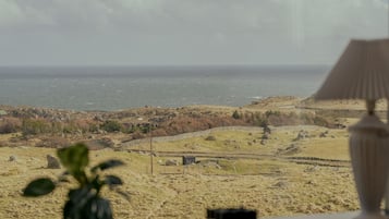 Enjoy the serene coastal view from this room, overlooking a sandy terrain and the ocean beyond a stone wall.