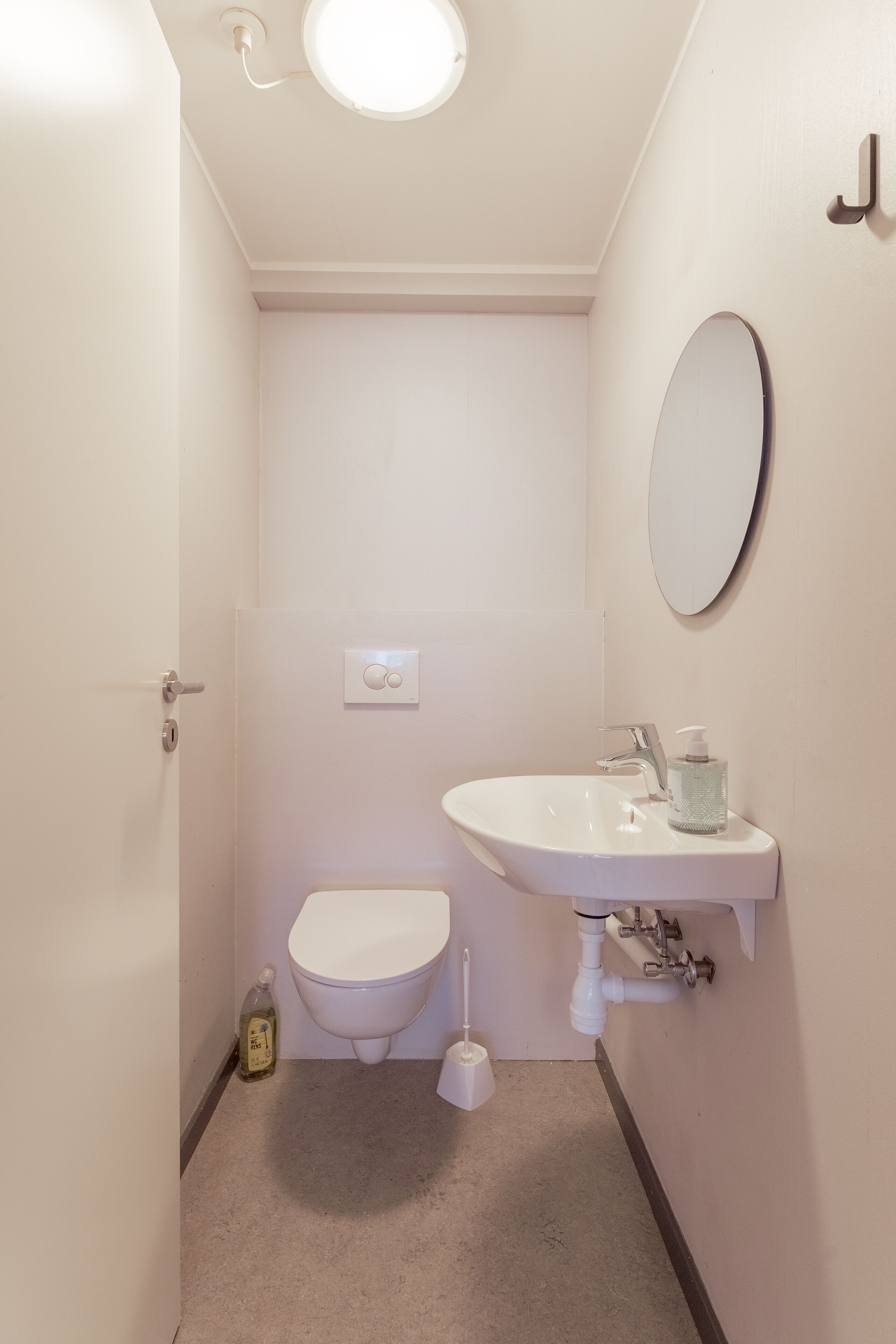 Ein kleines, weißes Badezimmer mit Toilette, Waschbecken und Spiegel.
