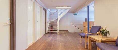 A hallway with wooden flooring, a staircase, and seating area with chairs and a table.