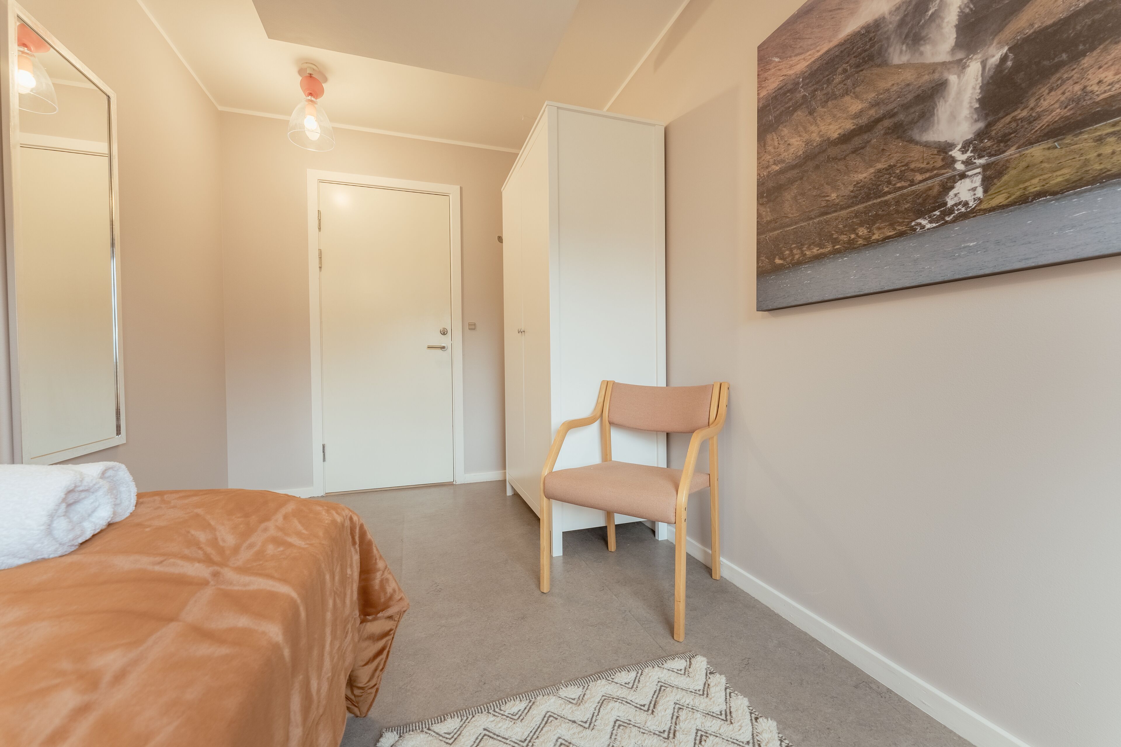 A bedroom with a bed, a chair, a wardrobe, and a painting on the wall.