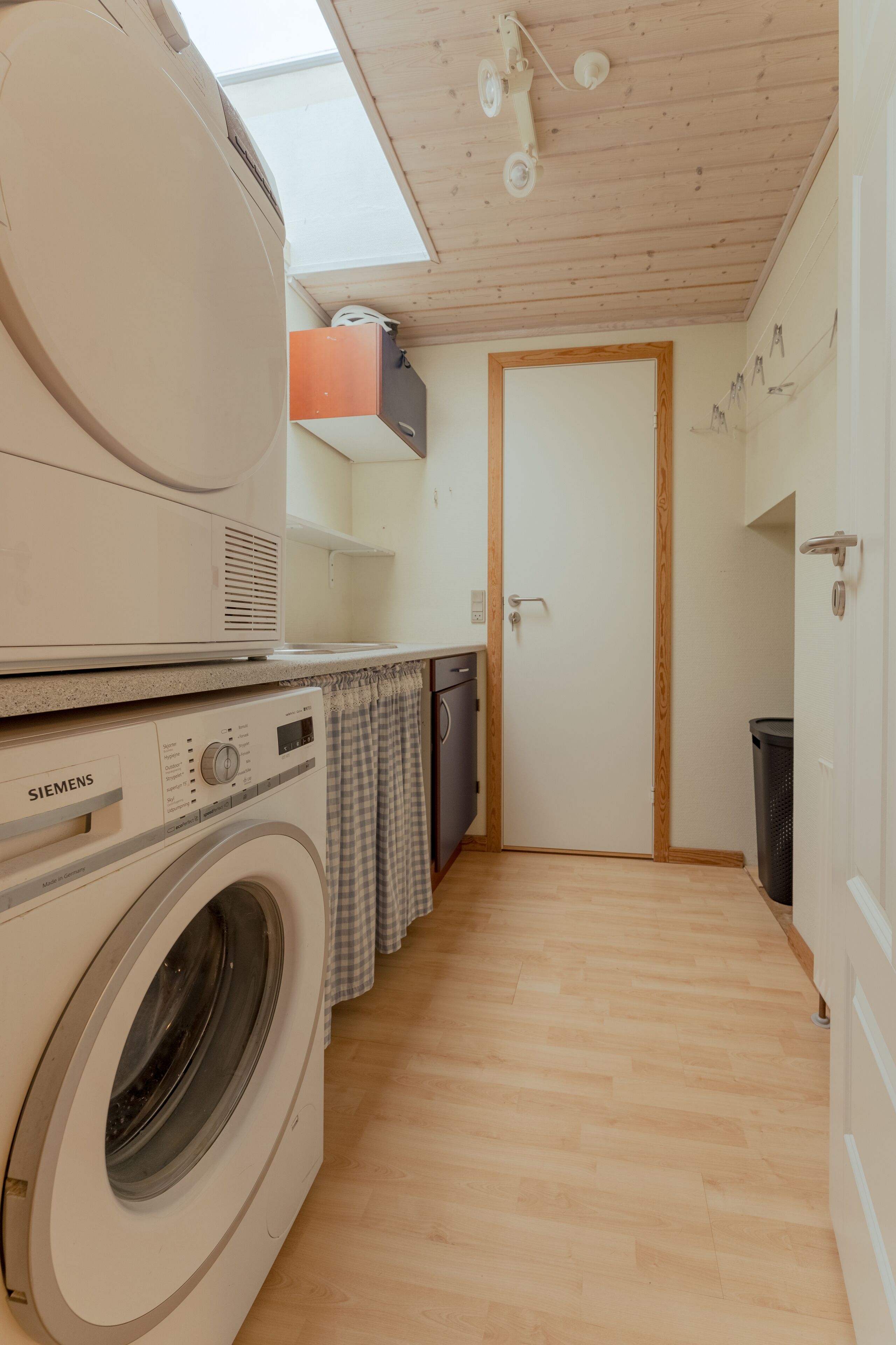 A compact laundry room with a Siemens washing machine, a dryer, a small sink, and a door leading to another room.