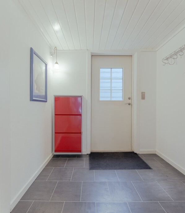 A hallway with a red cabinet, a door with a window, and a tiled floor. - Harbour View | 2Br | City Centre (Tórshavn)