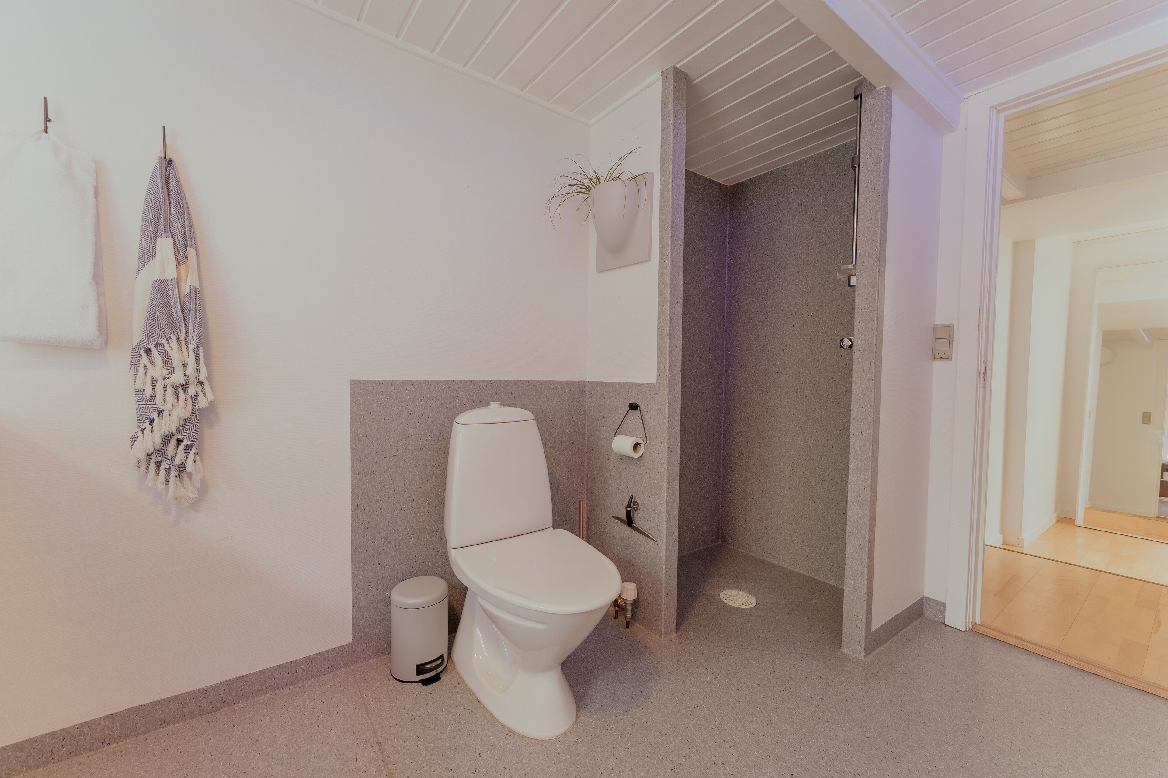 Ein modernes Badezimmer mit Toilette, Mülleimer, Handtuch und Duschbereich.