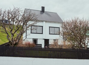Une maison moderne à deux étages, avec un toit noir, des murs blancs et une clôture en bois peinte en noir.