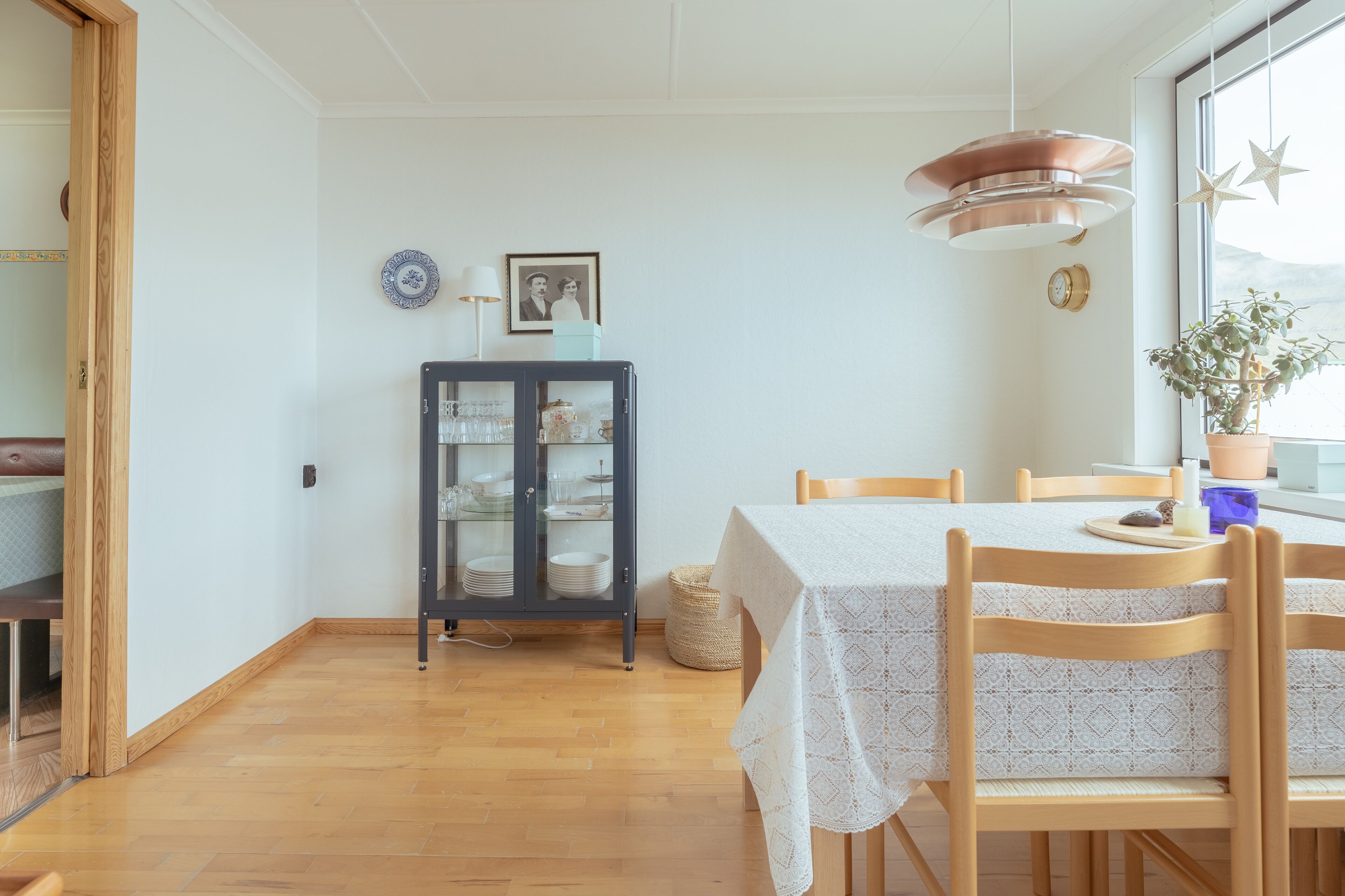A dining area with a table set for two, a cabinet with glass doors, and a window with a view.