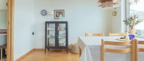 A dining area with a table set for two, a cabinet with glass doors, and a window with a view.