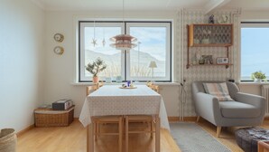 A dining area with a table set for four, a sofa, and a window with a view of mountains. - Serenity By The Sea | 3-Br House | Sea View (Sydrugota)