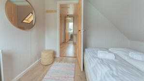 A bedroom with a bed, a round mirror, a woven stool, and a hallway leading to another room. - Serenity By The Sea | 3-Br House | Sea View (Sydrugota)