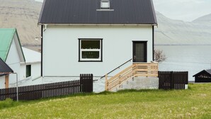 A white house with a black roof, a small window, and a wooden staircase leading to a door. - Serenity By The Sea | 3-Br House | Sea View (Sydrugota)