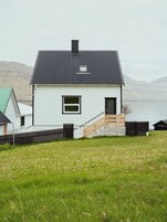 Ein weißes Haus mit schwarzem Dach, einem kleinen Fenster und einer Holztreppe, die zu einer Tür führt.