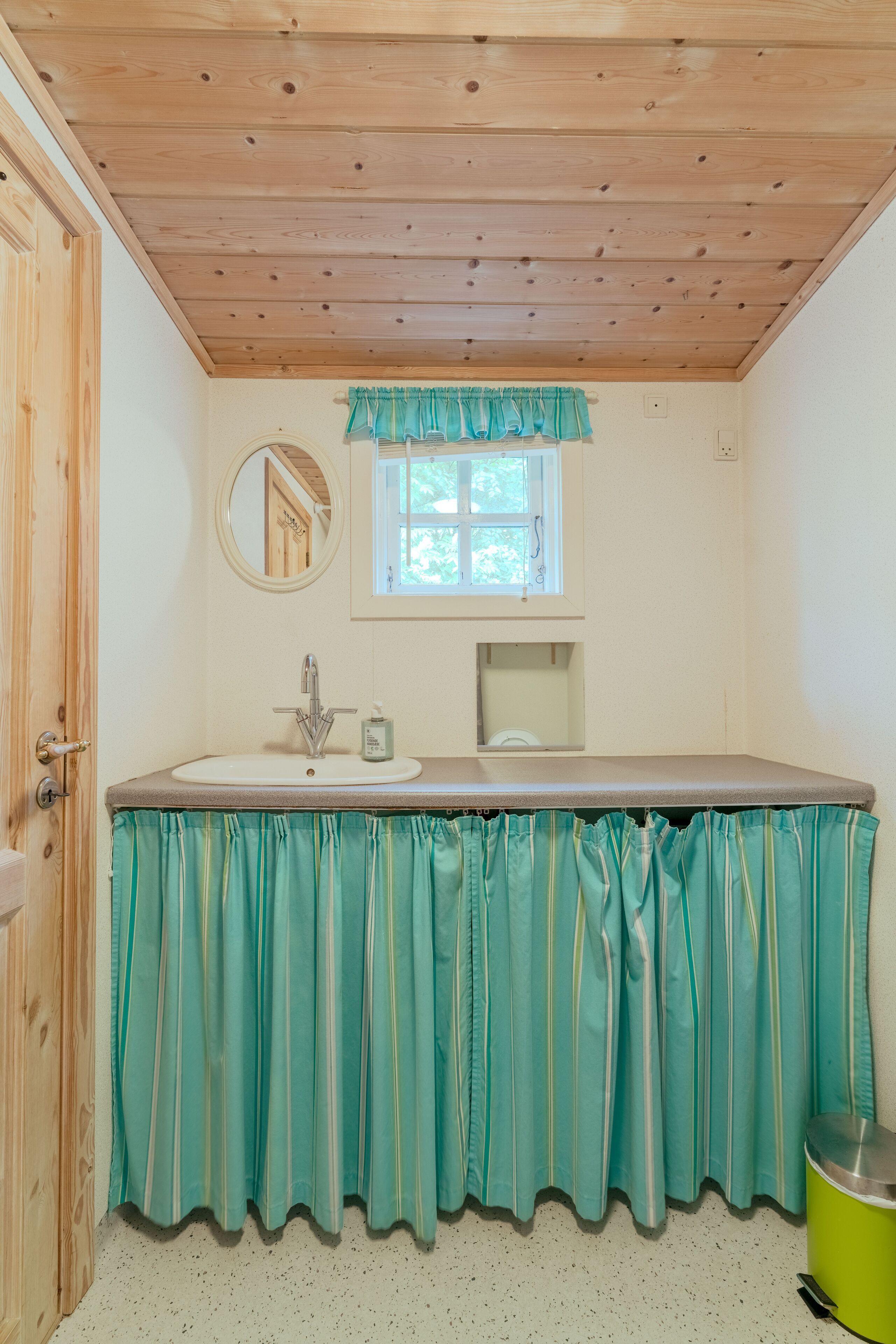 Une salle de bain avec un plafond en bois, un lavabo, un miroir, une fenêtre et un rideau vert.